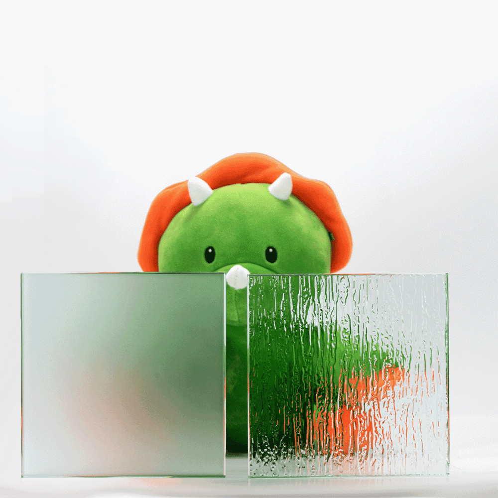 Custom glass samples showcasing frosted and textured options, with a playful green dinosaur plush toy in the background, highlighting shower doors, table tops, and mirrors.