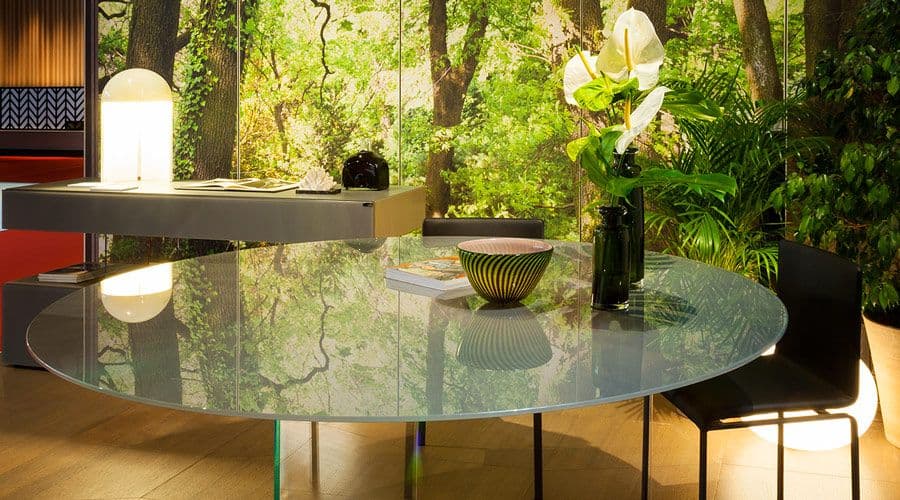 Custom glass table top with a reflective surface, surrounded by modern chairs and decor, showcasing a natural backdrop, ideal for home design featuring tempered glass and elegant aesthetics.