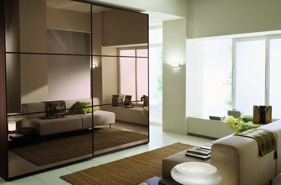 Modern living room featuring custom glass wall mirrors with a sleek beveled glass edge, enhancing the space's elegance alongside a cozy sofa and stylish decor.