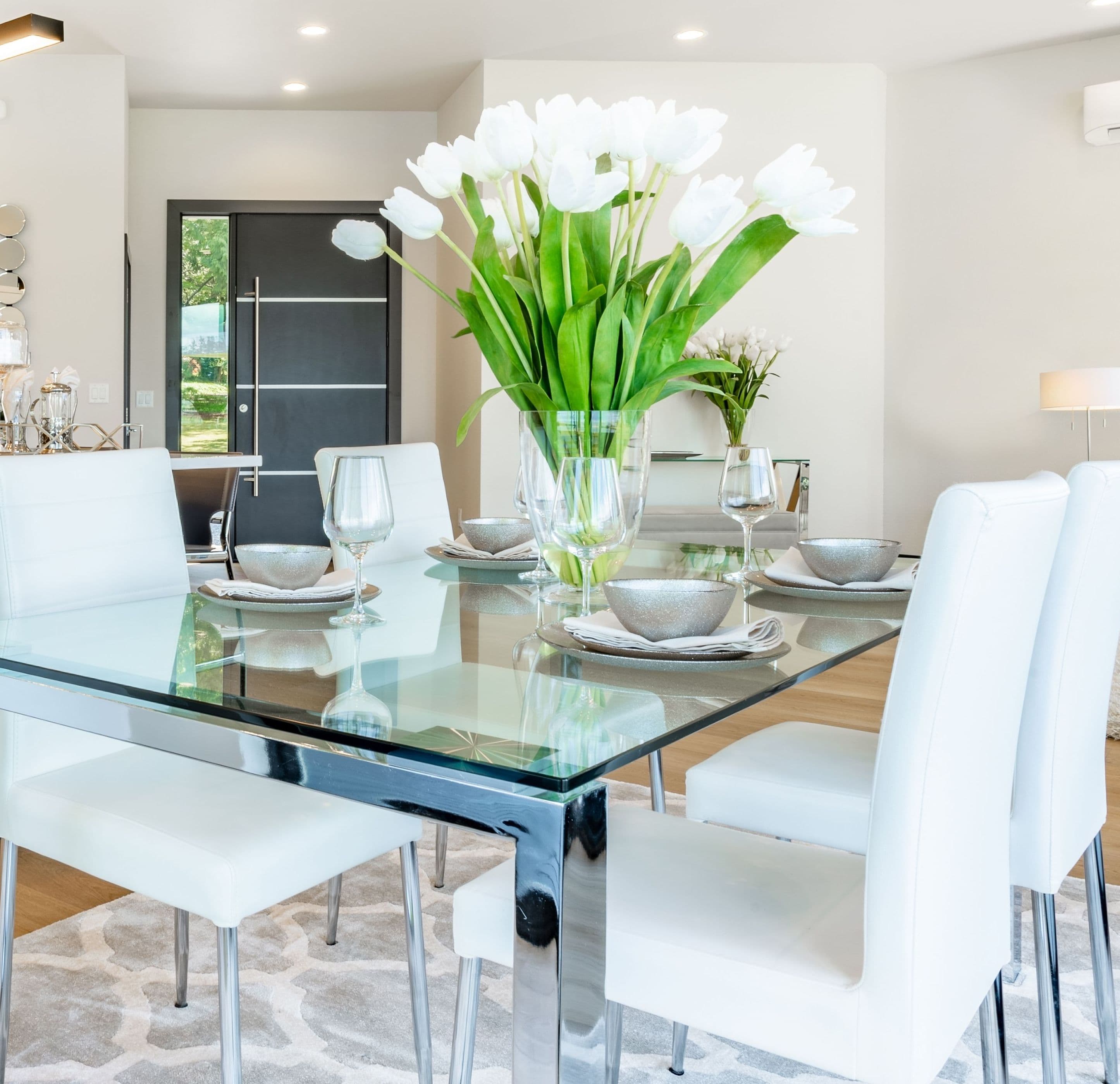 Modern dining room featuring a sleek glass table with a tempered glass top, stylish white chairs, decorative table settings, and elegant floral centerpiece, highlighting custom glass design.