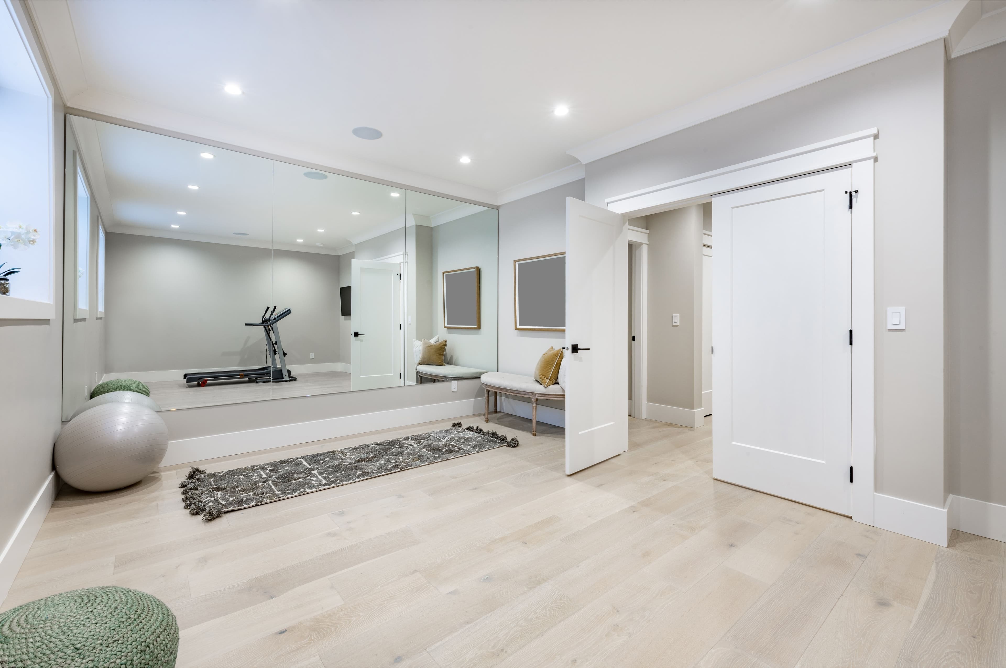 Modern gym space featuring a large custom mirror, sleek design elements, and a light-colored wooden floor, highlighting the versatility of custom glass solutions for interior aesthetics.