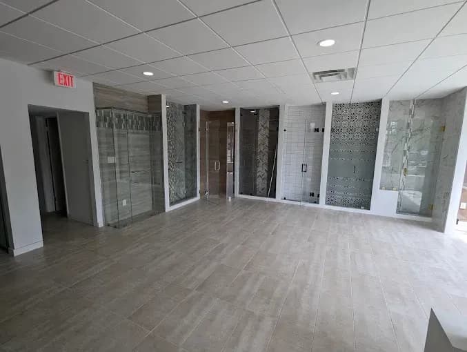 Showroom displaying various custom glass shower doors, table tops, and mirrors, featuring tempered glass and beveled glass edges.