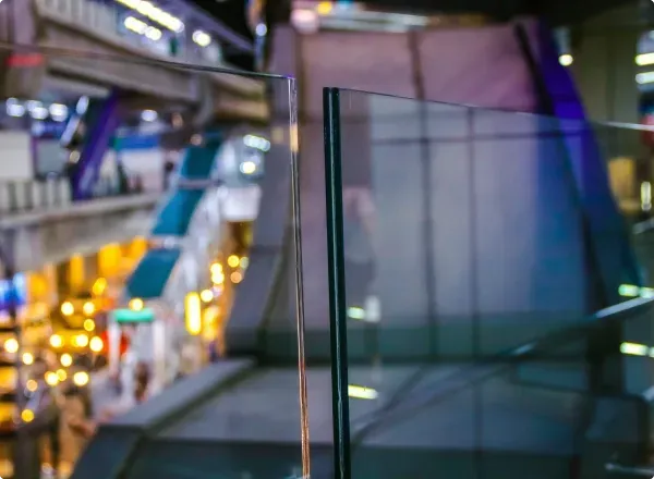 Custom tempered glass panel showcasing a beveled edge, with a blurred background of a modern shopping area, highlighting the versatility for shower doors, table tops, and mirrors.