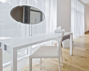 Modern white desk with a custom oval mirror reflecting natural light, surrounded by large windows, showcasing stylish interior design, perfect for spaces featuring custom glass and tables.