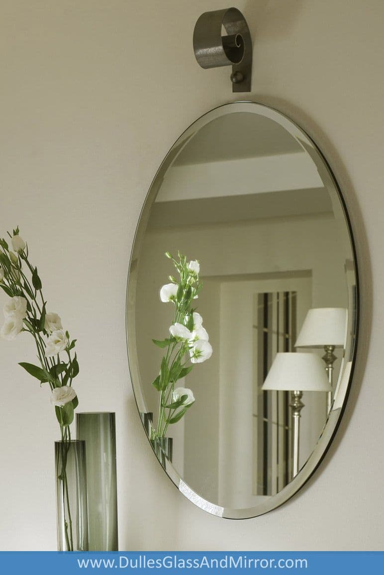 Oval mirror with beveled glass edge, complementing decorative vase and flowers, showcasing custom glass craftsmanship for home decor.