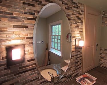 Custom oval mirror with beveled glass edge in a modern bathroom featuring stone tile, showcasing premium design for custom glass solutions.