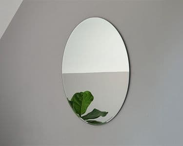 Oval mirror with a beveled glass edge reflecting a green plant, showcasing custom glass design suitable for home decor.