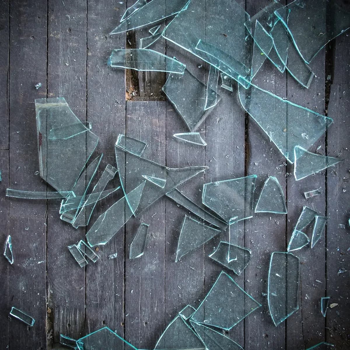 Shattered pieces of tempered glass on a wooden surface, highlighting custom glass applications like shower doors, table tops, and mirrors.