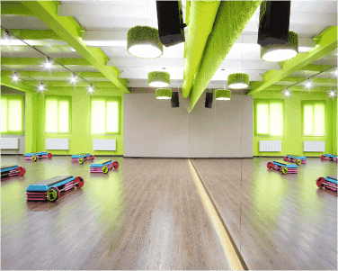 Spacious fitness studio with vibrant green walls, featuring a large custom glass mirror and ample natural light, showcasing modern design elements ideal for shower doors, table tops, and beveled glass edge applications.