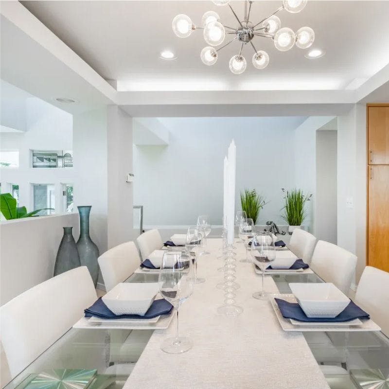 Glass table tops with White chairs and chandelier in dining room