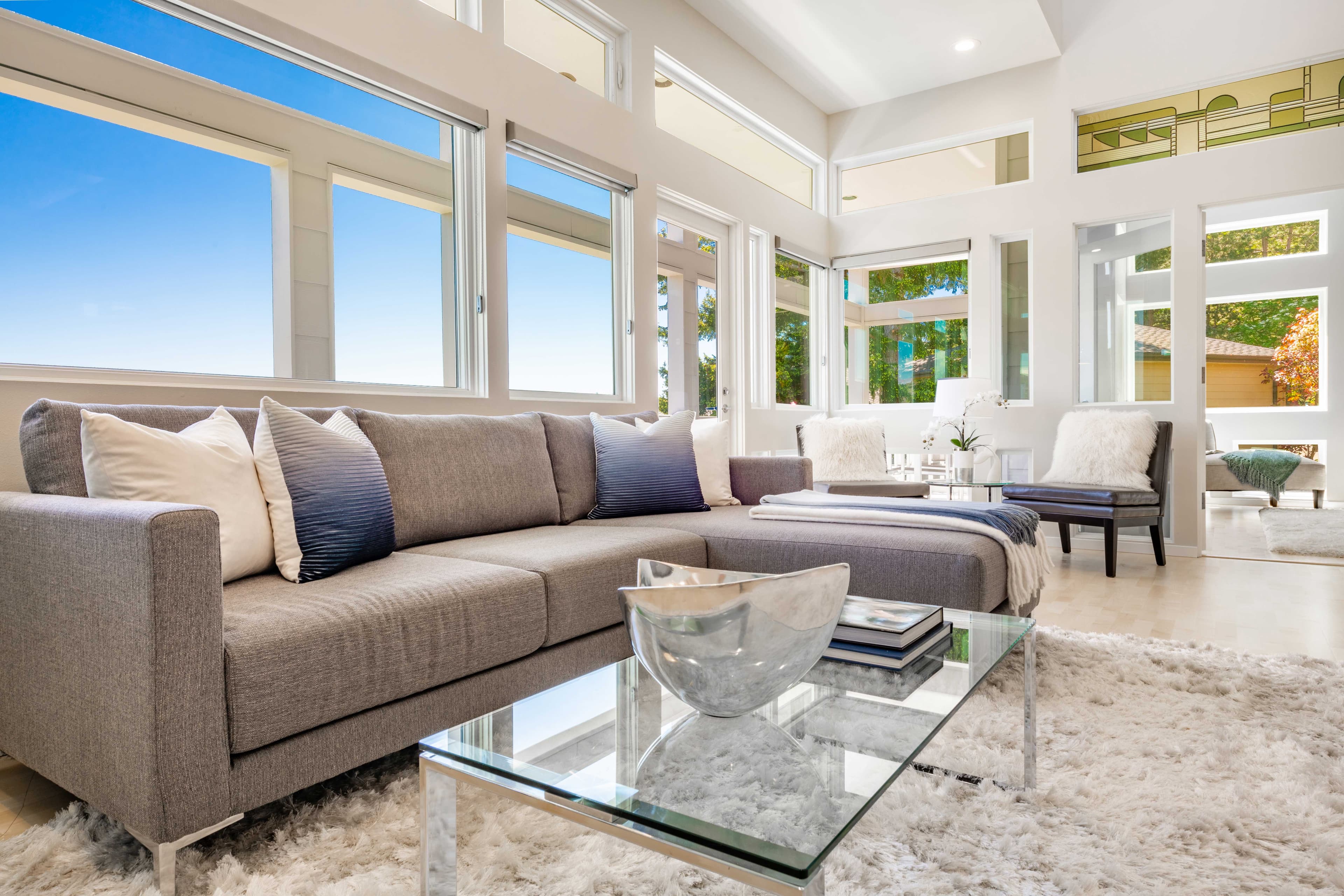 Modern living room featuring a sleek glass table top, enhancing the space with reflections, complemented by abundant natural light through large windows, showcasing custom glass design elements ideal for interiors.