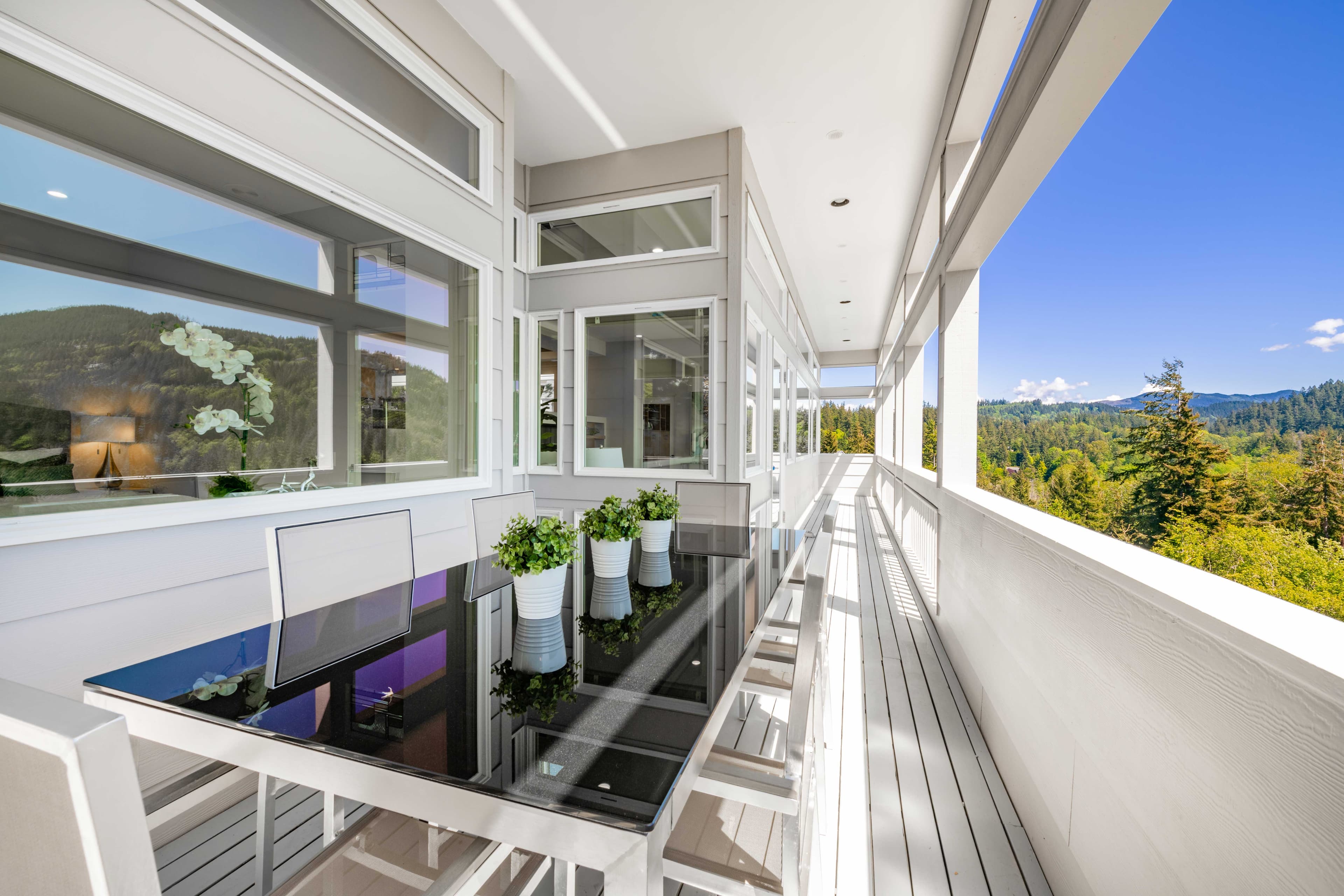 Modern outdoor space featuring a sleek glass table top surrounded by stylish chairs, showcasing custom glass solutions for entertaining while enjoying scenic views.