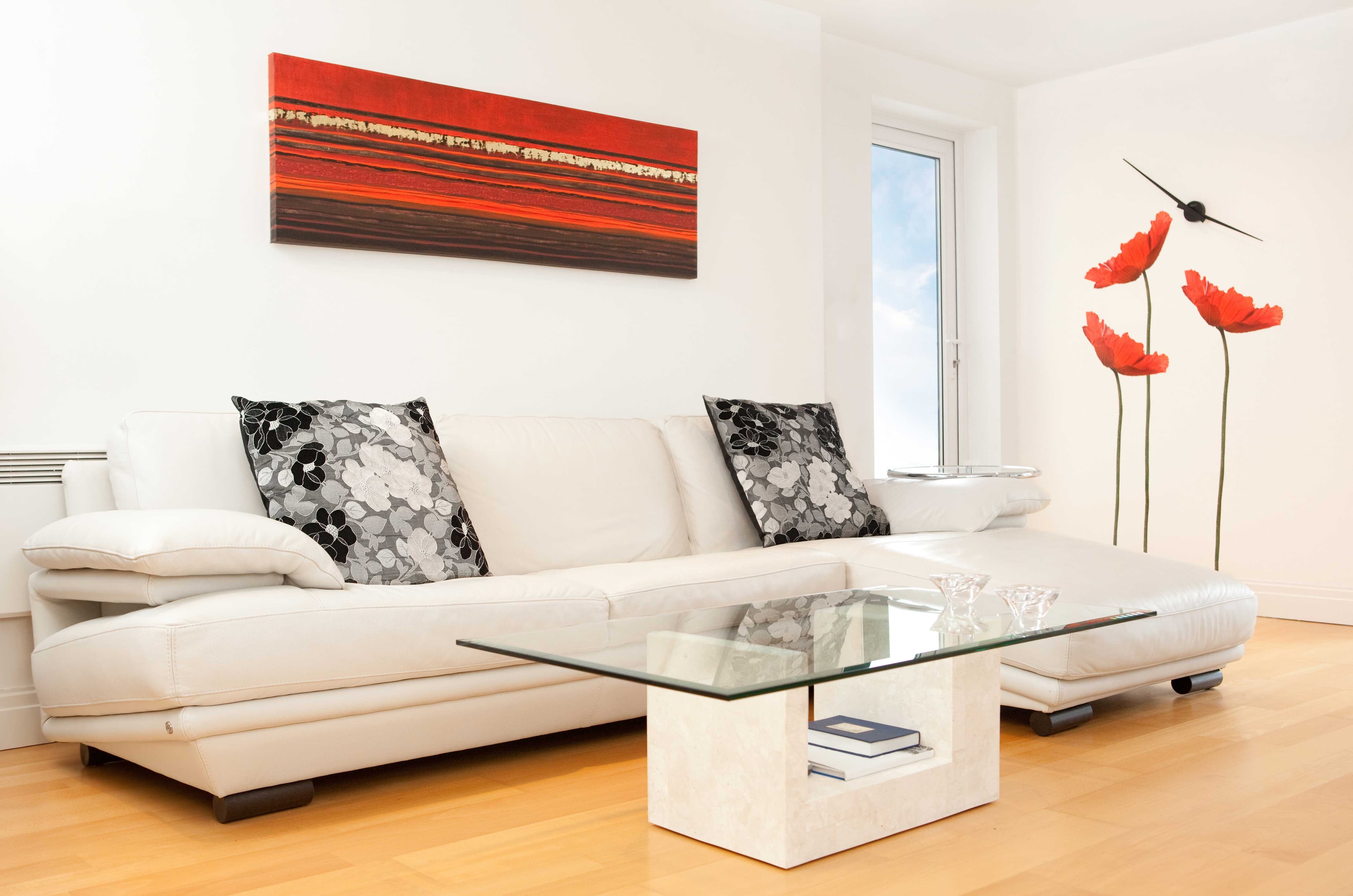 Modern living room featuring a stylish glass coffee table on a wooden floor, complemented by a white leather sofa and decorative pillows, showcasing the elegance of custom glass design.