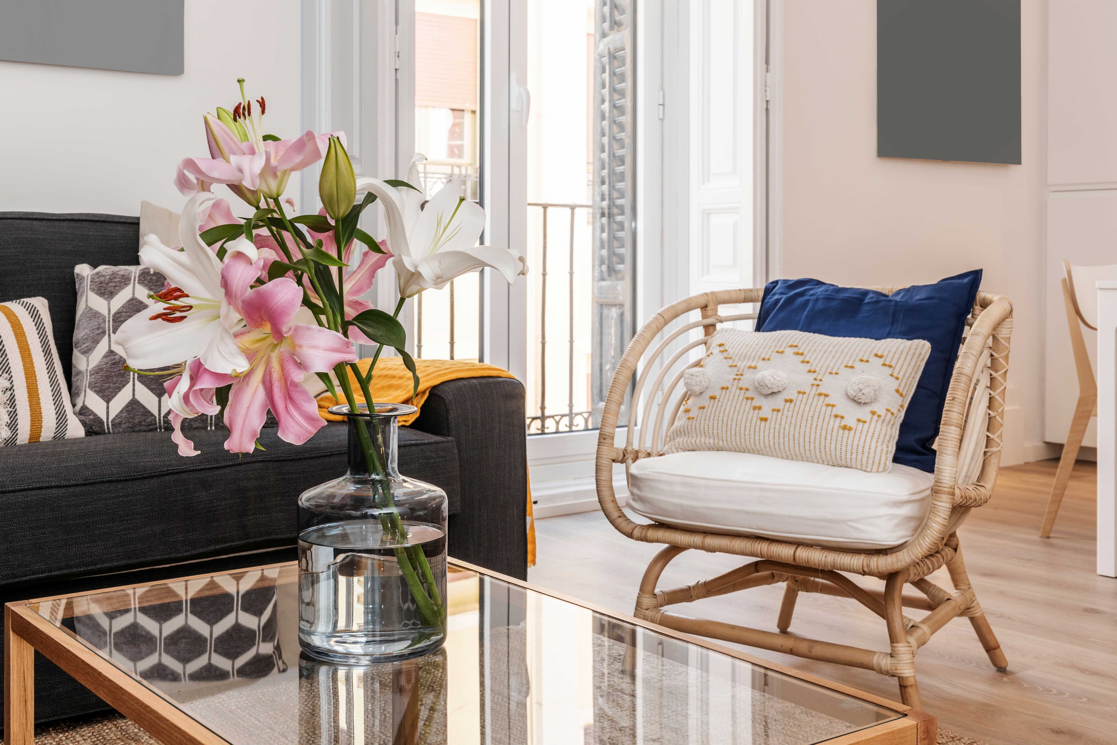 Living room scene featuring a glass table top reflecting flowers, complemented by a cozy sofa with decorative pillows; ideal for custom glass solutions, including tempered and beveled glass edges.