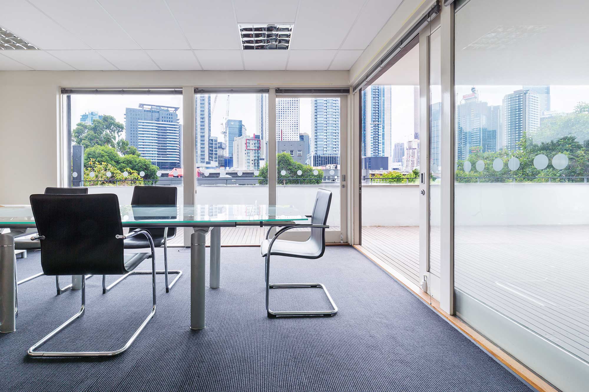 Modern conference room featuring a glass table, surrounded by sleek chairs, showcasing custom glass elements with a view of the city skyline through large glass sliding doors.