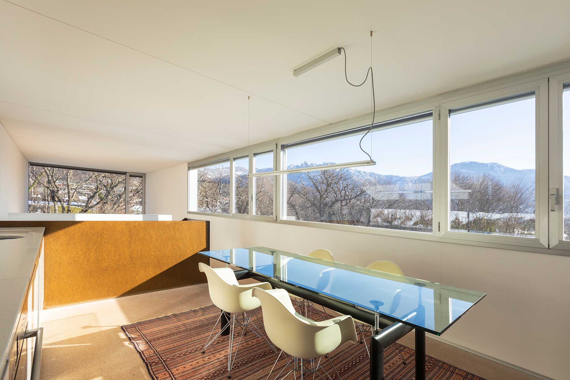 Modern interior featuring a sleek glass table top, surrounded by stylish chairs, with large windows offering a scenic view, highlighting the use of custom glass in contemporary design.
