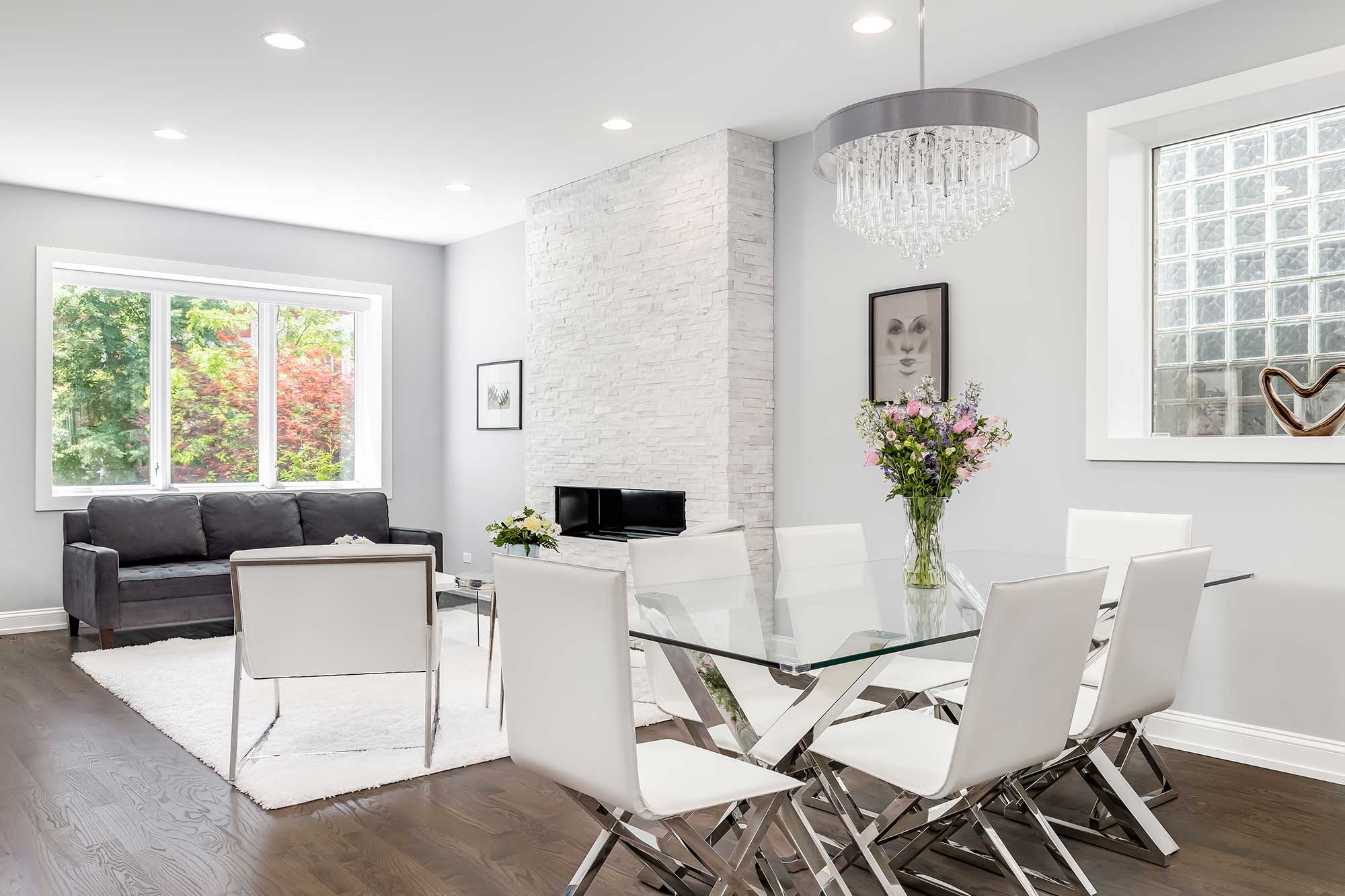 Elegant dining area featuring a custom glass table top, surrounded by modern white chairs, and complemented by decorative mirrors and a stylish chandelier, highlighting a minimalist design aesthetic.