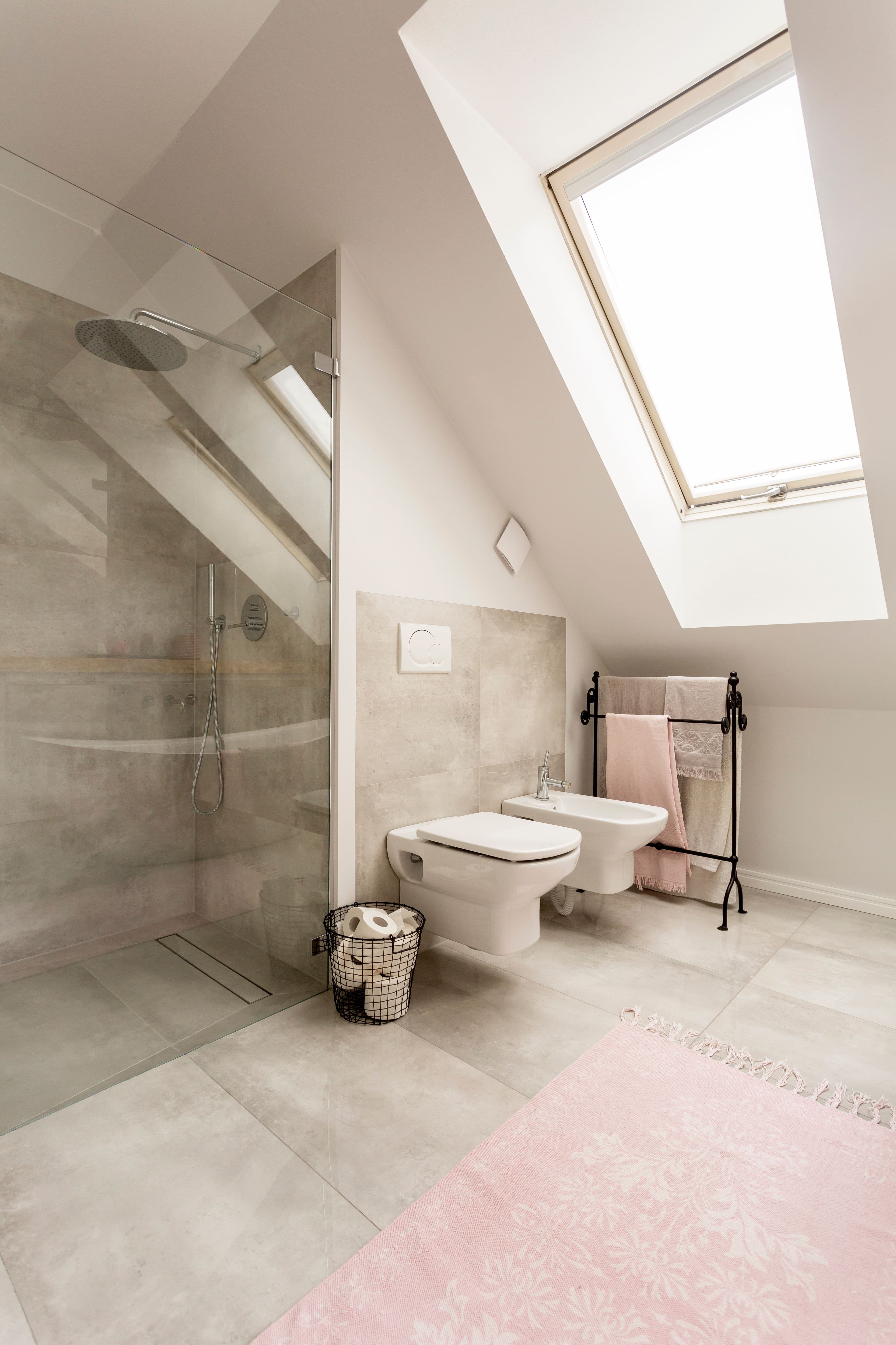 Modern bathroom featuring a transparent shower door, sleek fixtures, and a soft pink rug, showcasing custom glass solutions ideal for shower doors and mirrors.