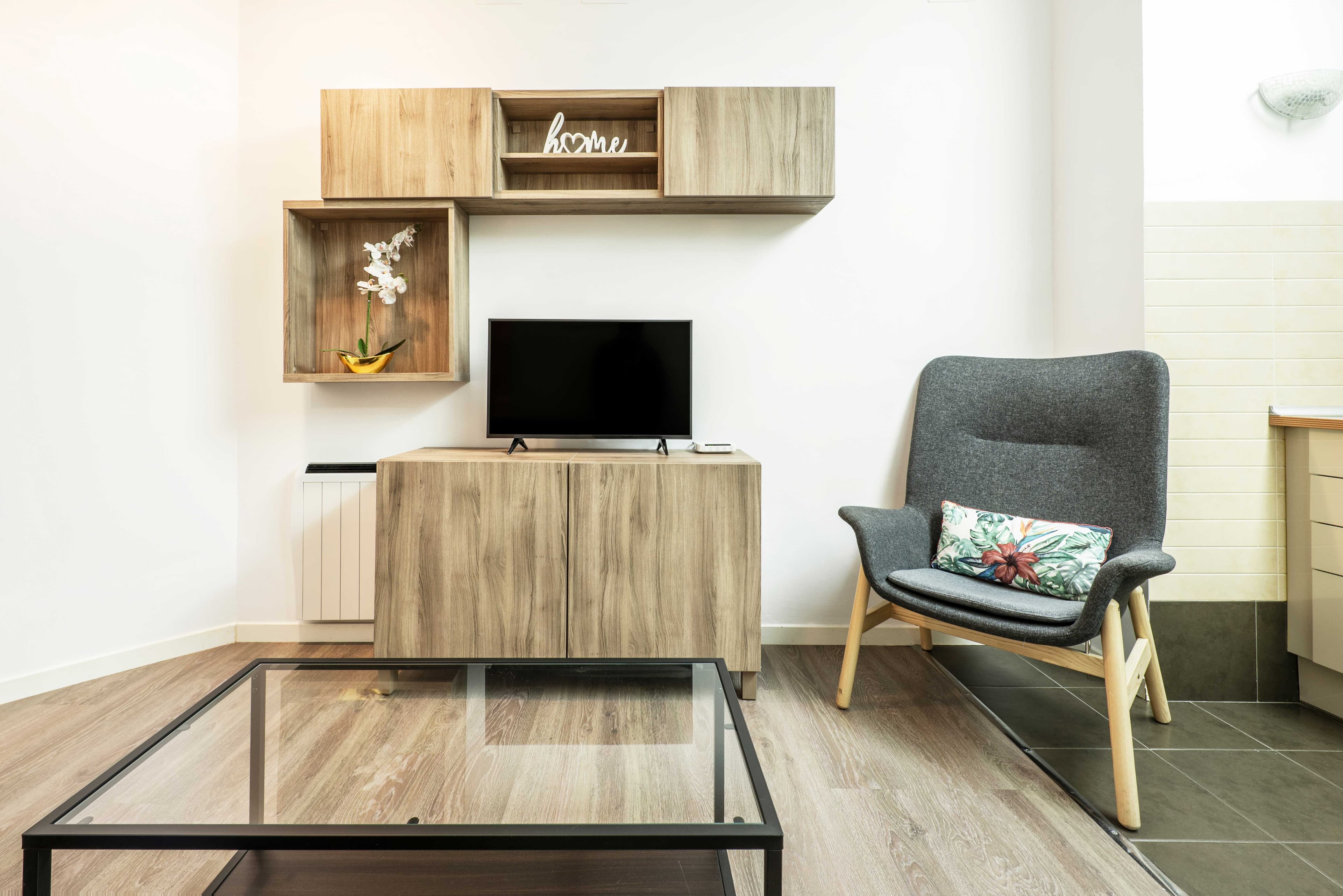 Stylish living room featuring a glass coffee table with a modern design, complemented by a wooden TV stand, decorative wall shelves, and a cozy chair, showcasing custom glass solutions ideal for shower doors, table tops, and mirrors.