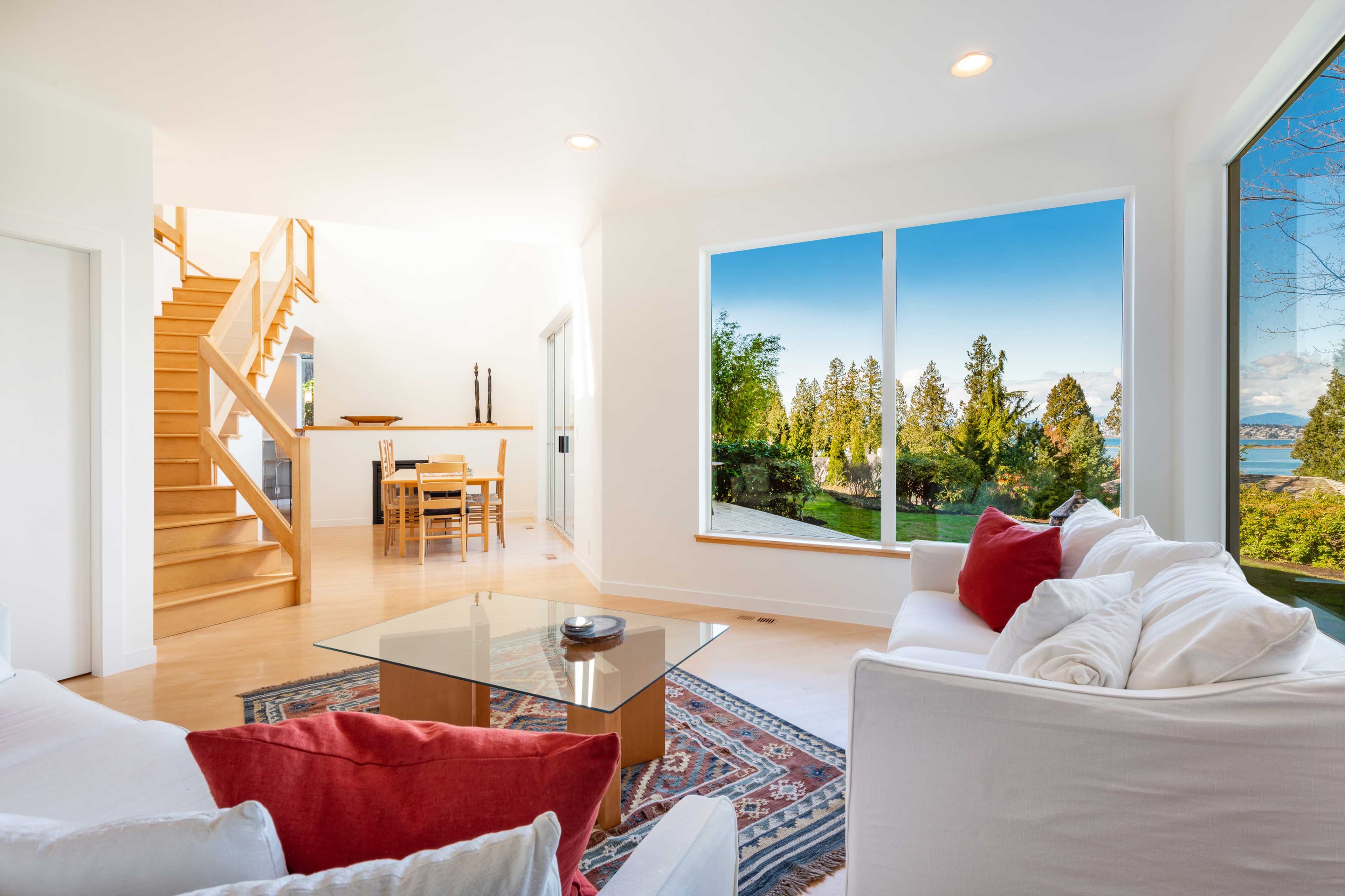 Modern living room featuring a glass coffee table with a scenic view through large windows, showcasing natural light and elegance, ideal for custom glass solutions like shower doors, tempered glass, and beveled glass edges.