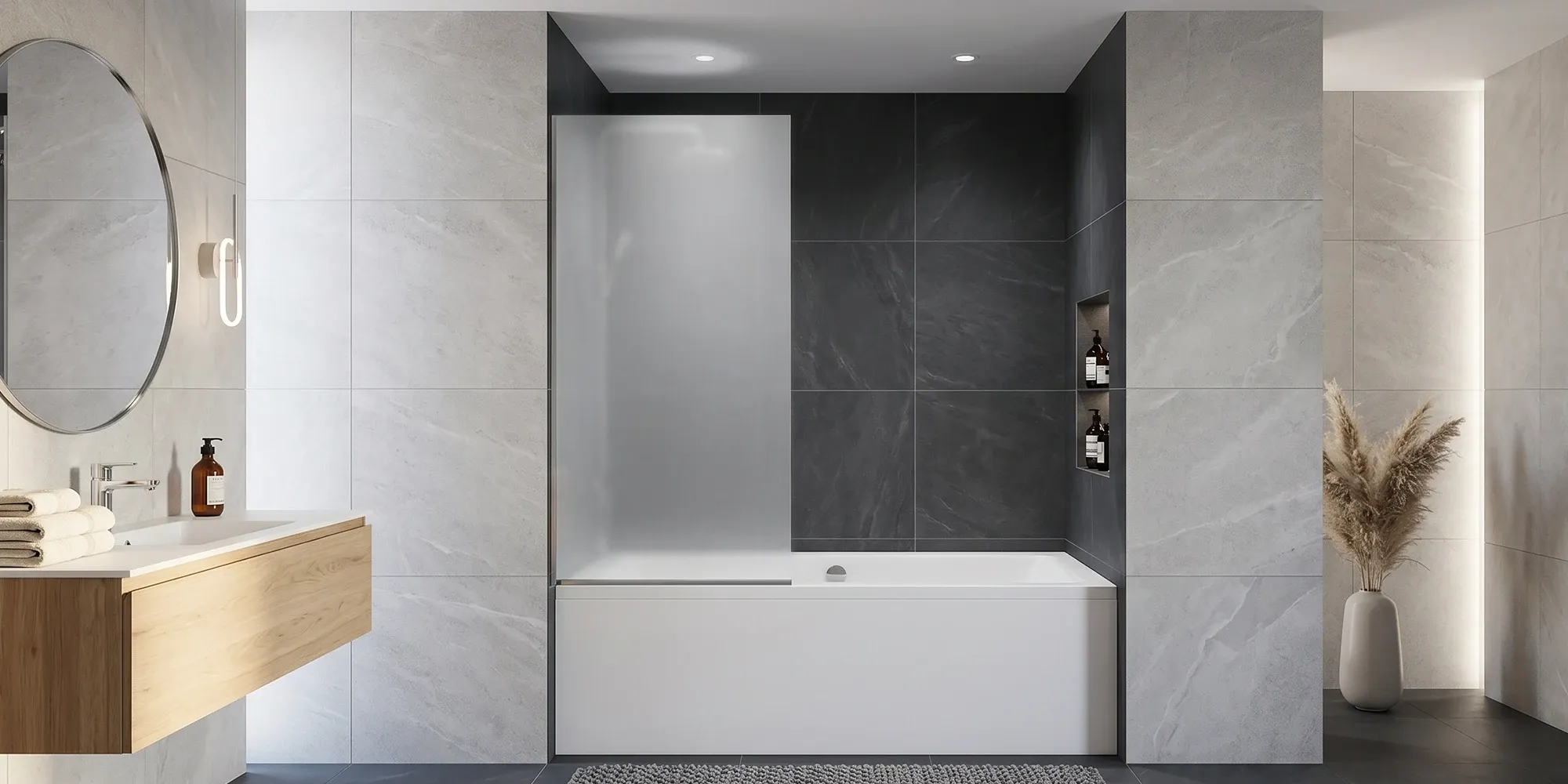 Modern bathroom featuring a white bathtub with a frosted glass splash guard, a floating wood vanity with a round mirror, and grey stone-textured wall tiles.
