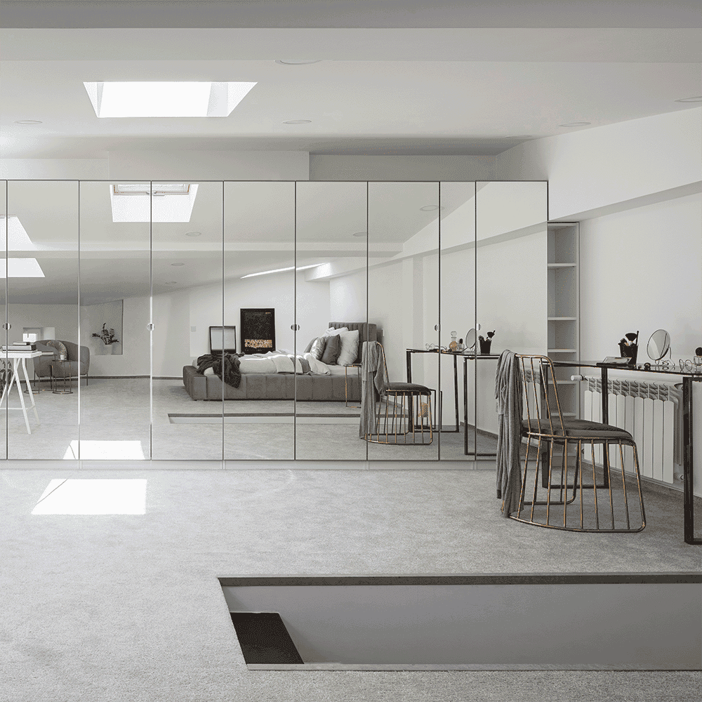 Modern interior featuring custom glass mirrors reflecting a stylish living space, complemented by sleek furniture and a cozy atmosphere. Ideal for showcasing custom glass solutions like shower doors and table tops.