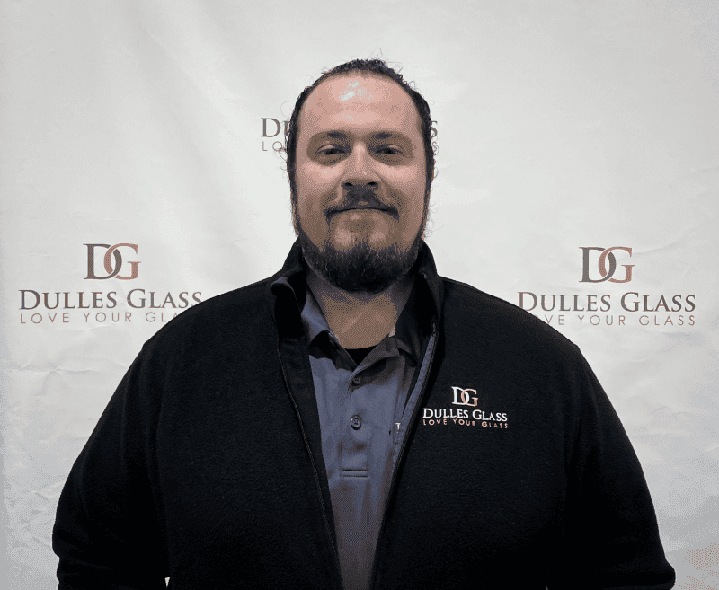 Employee of Dulles Glass showcasing custom glass options, including shower doors, table tops, mirrors, tempered glass, and beveled glass edge, with branding in the background.