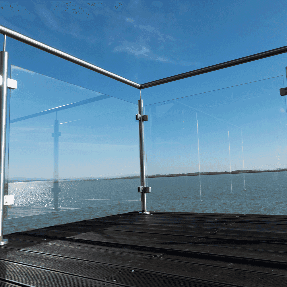 Modern glass railing overlooking a serene body of water, highlighting custom glass solutions suitable for shower doors, tempered glass, and elegant designs.
