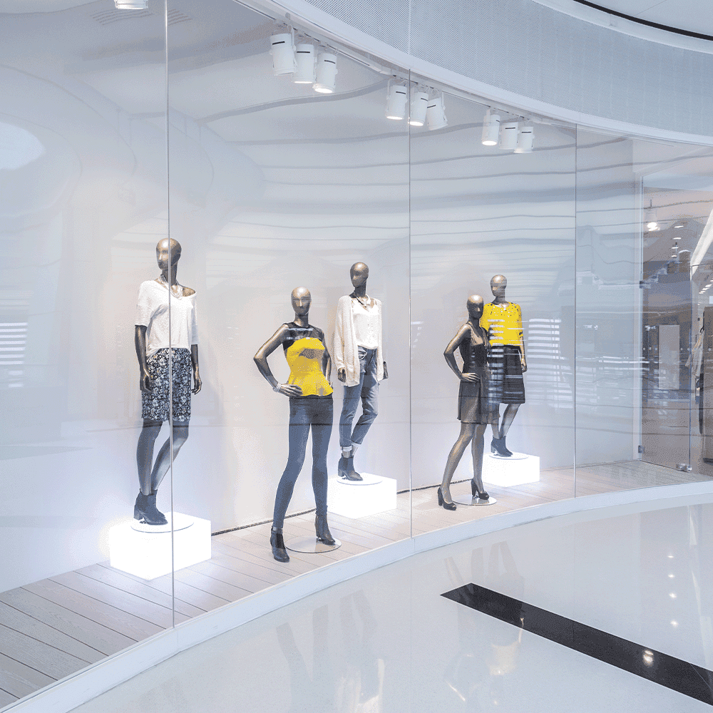 Modern retail display featuring mannequins behind clear custom glass panels, highlighting shower doors, table tops, and mirrors.
