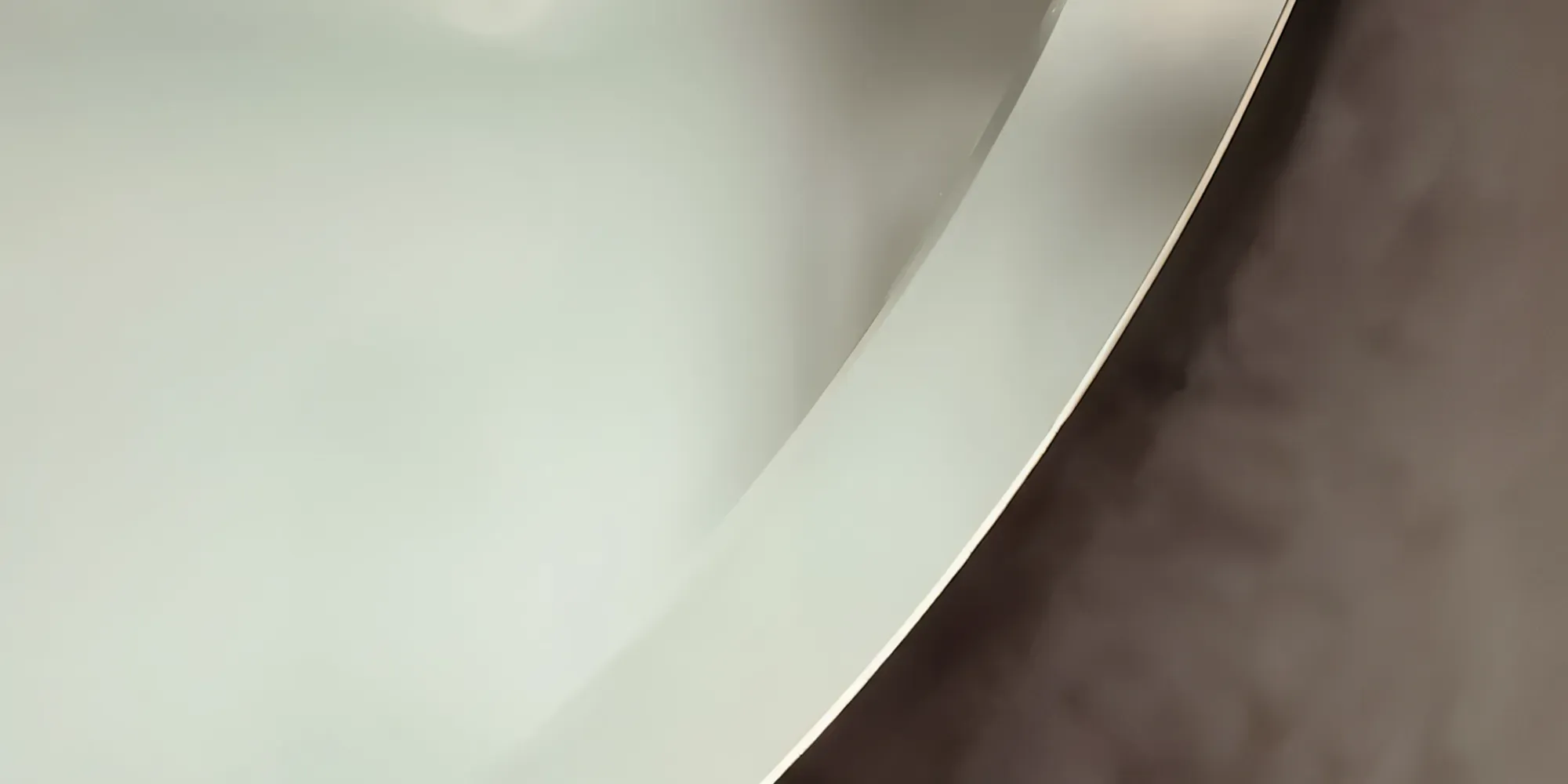 An abstract macro image showing the sleek, curved, and polished beveled edge of a mirror.