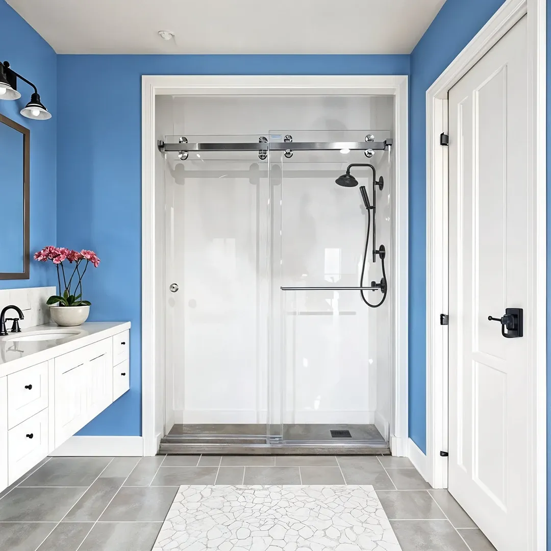 A striking bathroom with bold blue walls, featuring a walk-in shower with a sliding glass door on a chrome barn-door track and contrasting matte black fixtures.