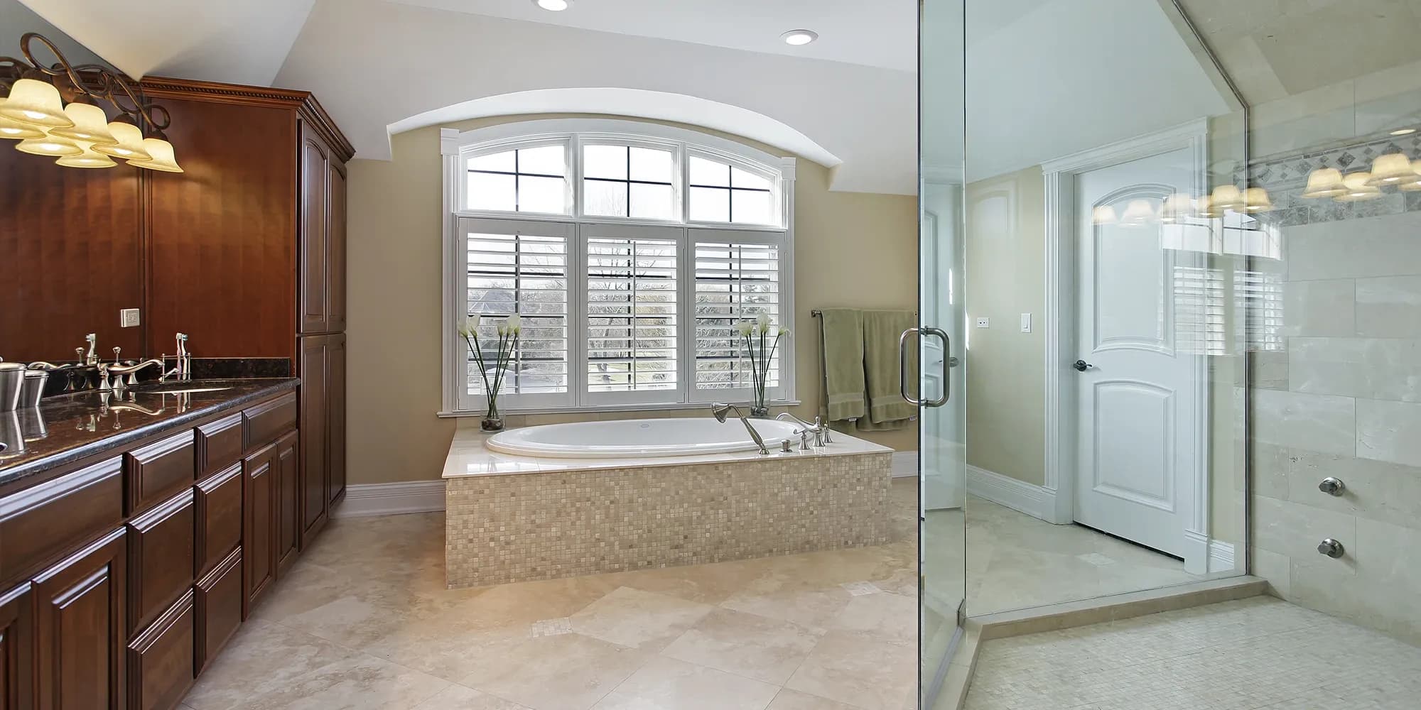 An elegant bathroom in a historic home featuring a frameless glass shower, a large soaking tub with a mosaic tile surround, and dark cherry wood cabinetry.