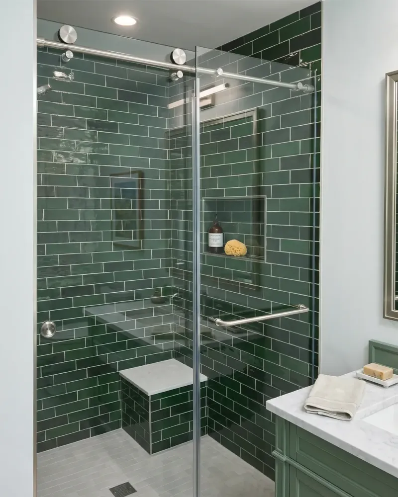 Sliding glass shower door with green subway tile, built-in bench and chrome hardware