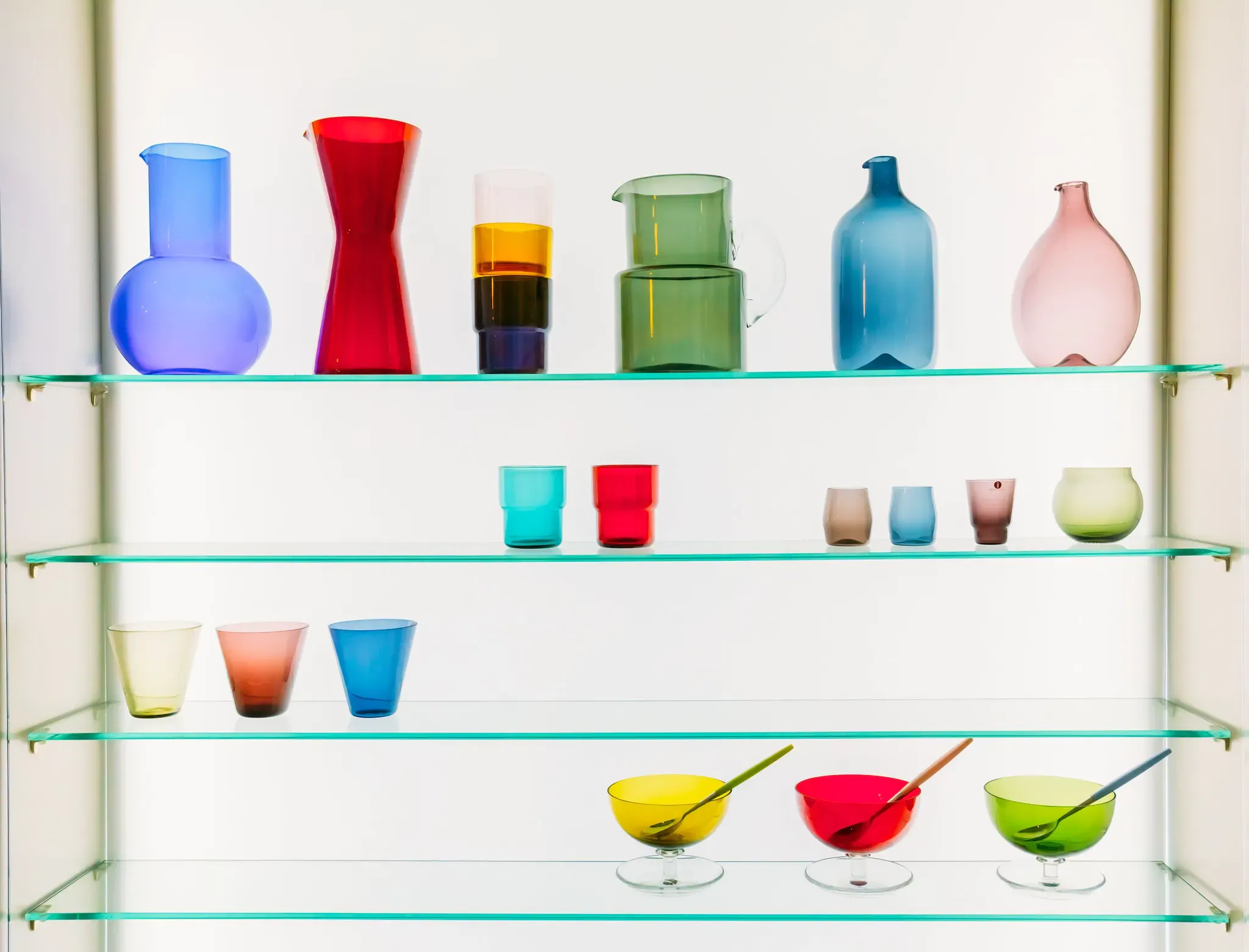 Colorful glassware displayed on custom glass shelves, showcasing various shapes and sizes, ideal for modern home decor with options for tempered glass and beveled edges.
