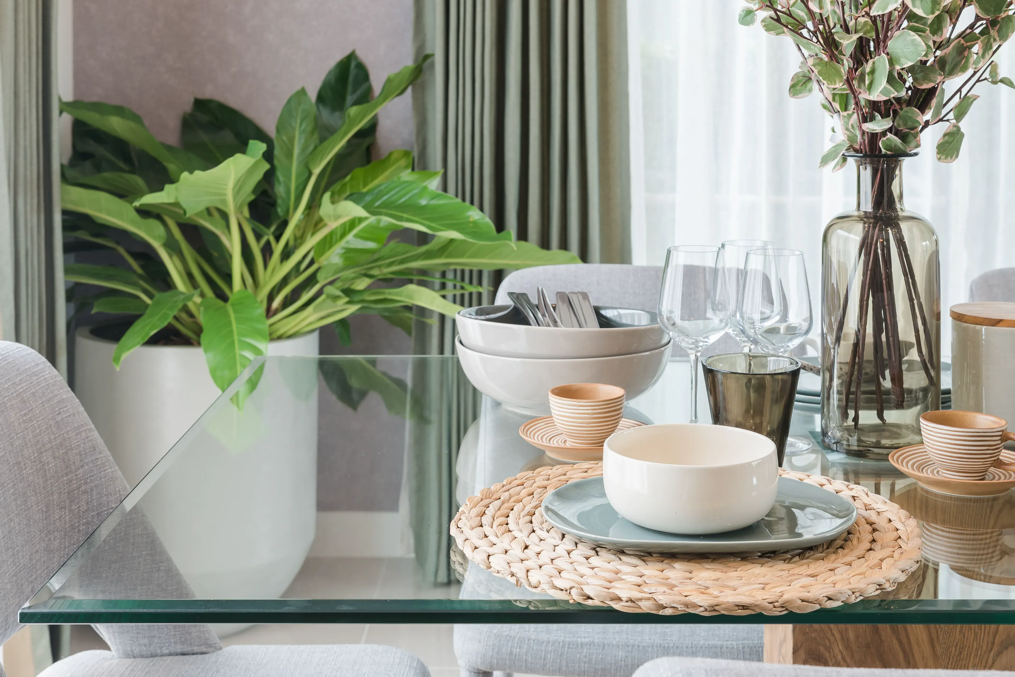 Custom glass table top with beveled edges, surrounded by elegant dinnerware, plant decor, and glassware, highlighting the versatility of tempered glass in home settings.
