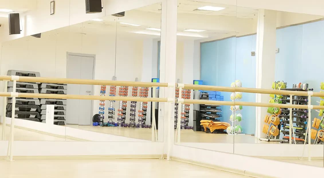 Mirrored wall in a fitness studio reflecting exercise equipment, showcasing custom glass solutions, including tempered and beveled glass edges.