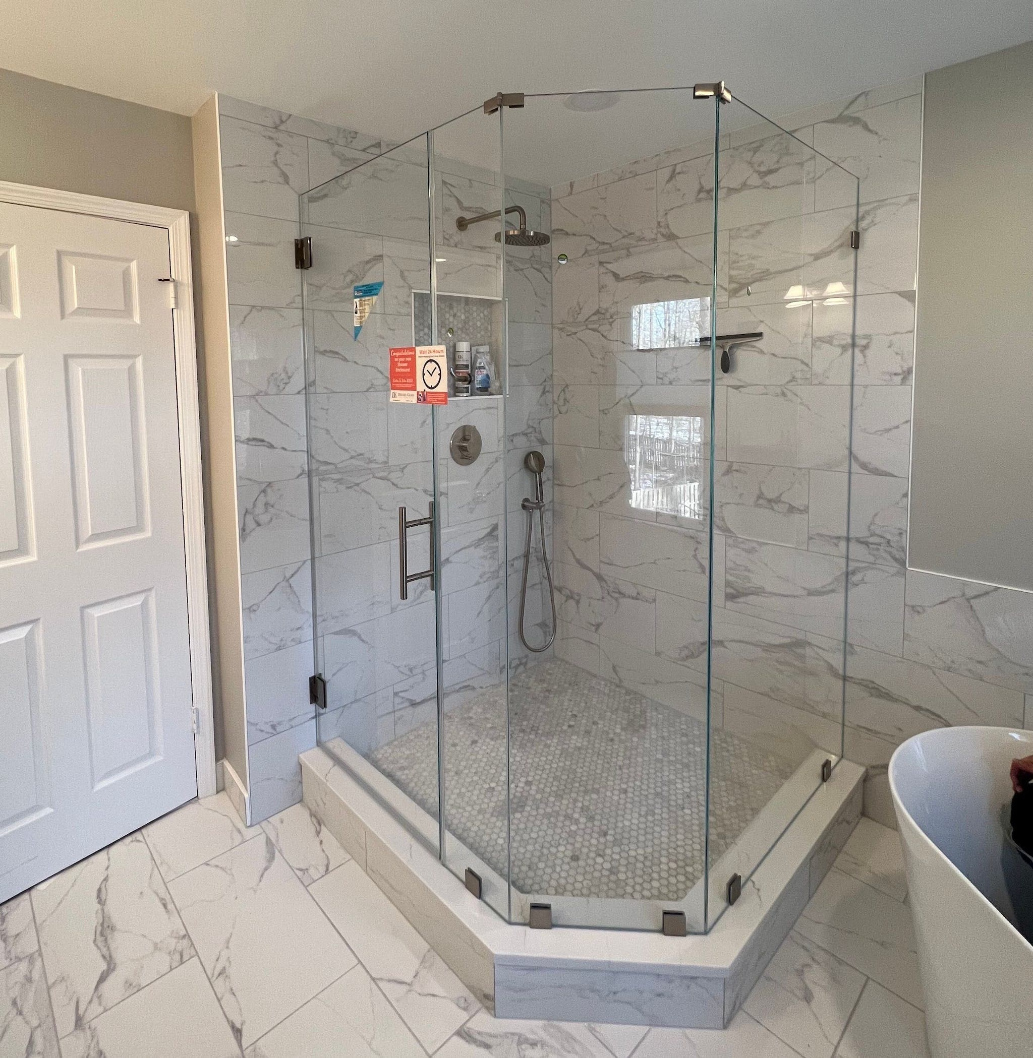 Custom shower doors with tempered glass and beveled edges in a modern bathroom featuring marble tiles and a sleek design.